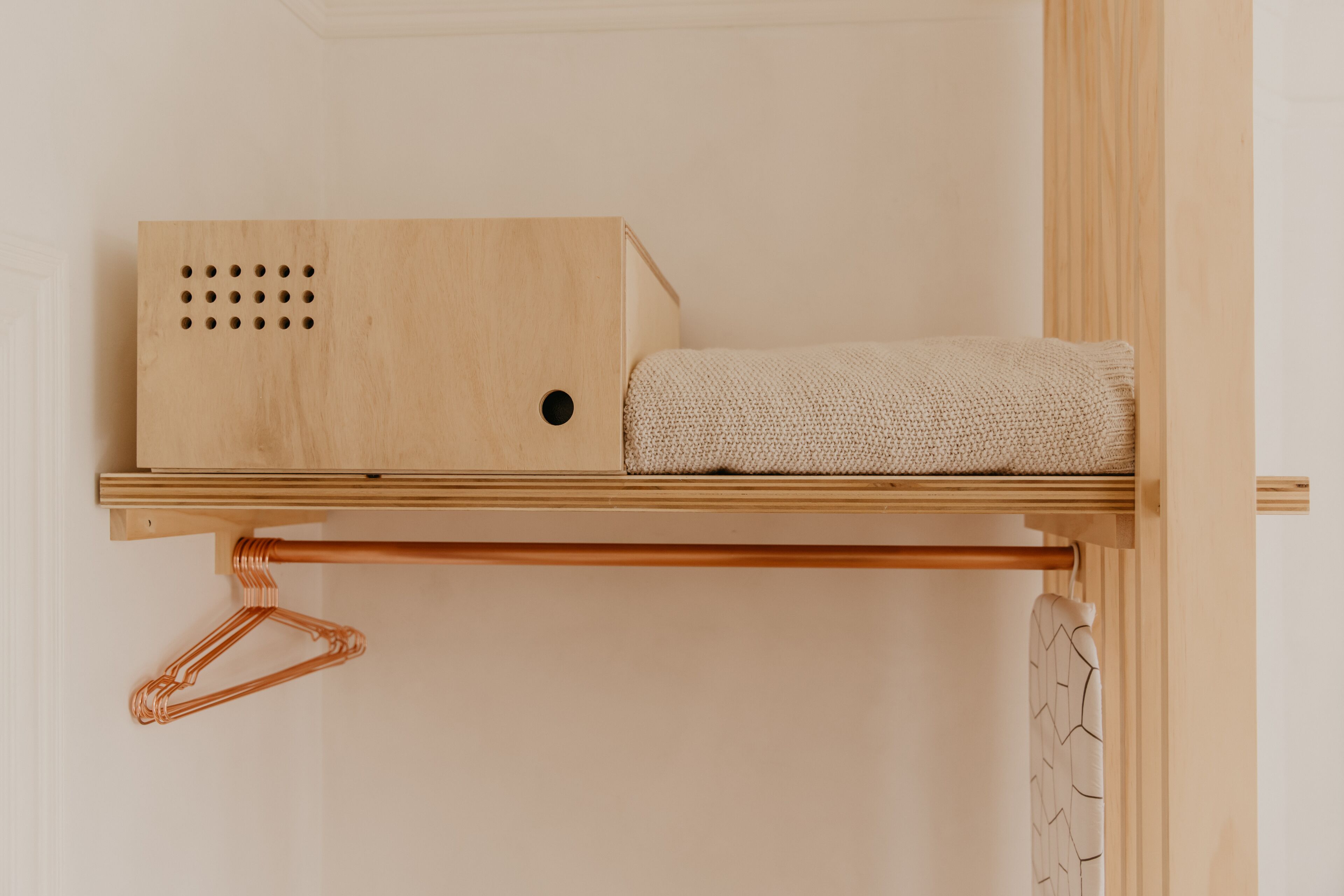 A wooden shelf with a hanging copper hanger and a folded blanket.