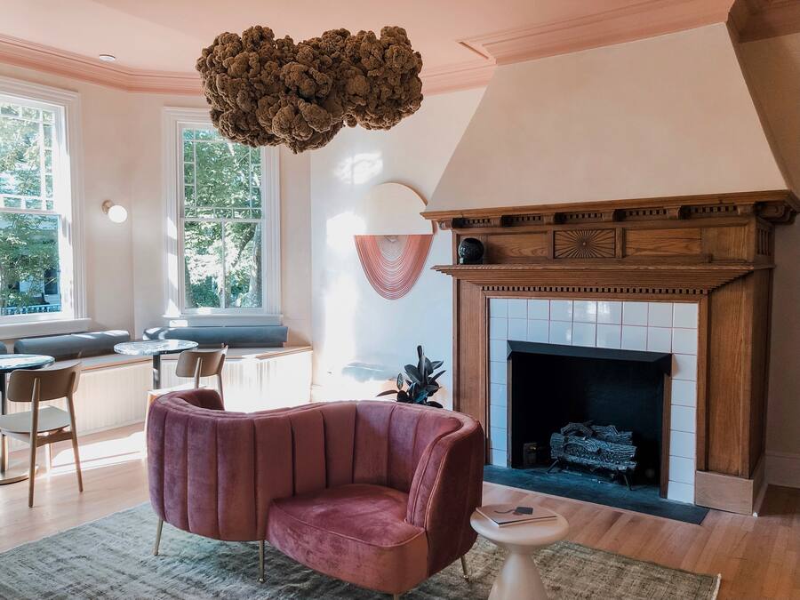 A living room with a fireplace, a plush red armchair, a round coffee table, and a large window with a view of trees.