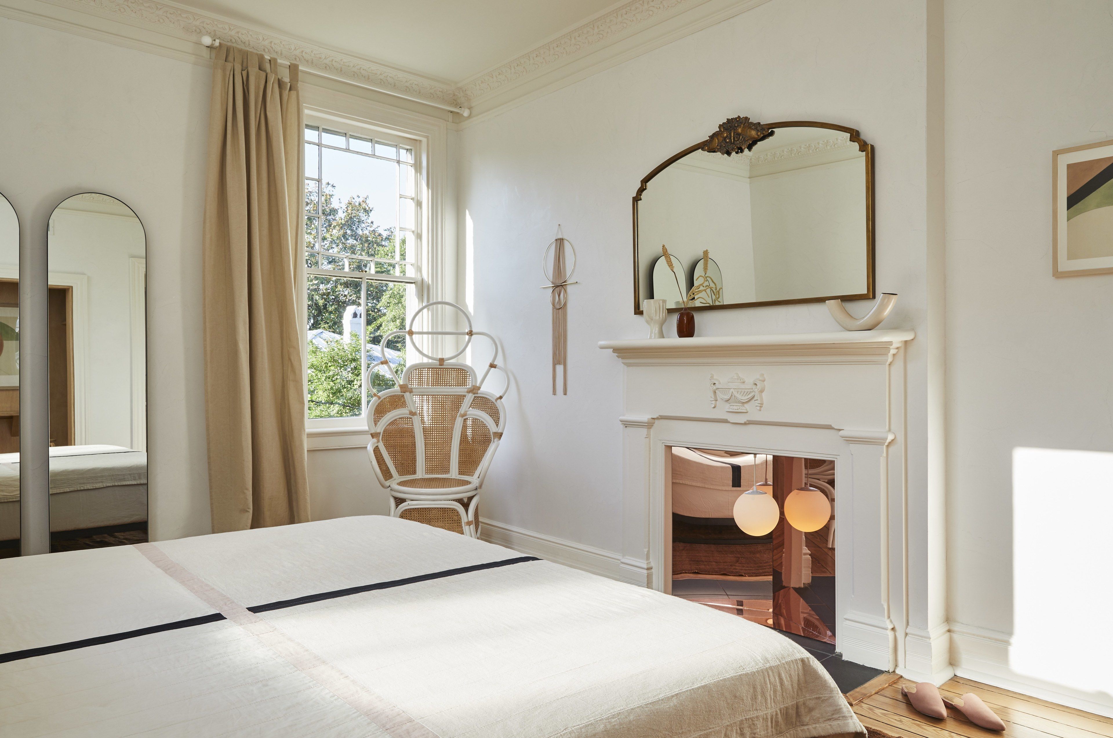 A bedroom with a bed, a chair, a fireplace, and a large mirror.