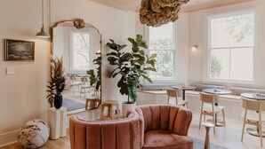 A modern interior with a plush velvet armchair, a large mirror, and a potted plant. - Dreamers BNB (Wilmington)