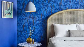 A bedroom with a bed, a round table with a vase and a lamp, and a wall with a blue leafy pattern.