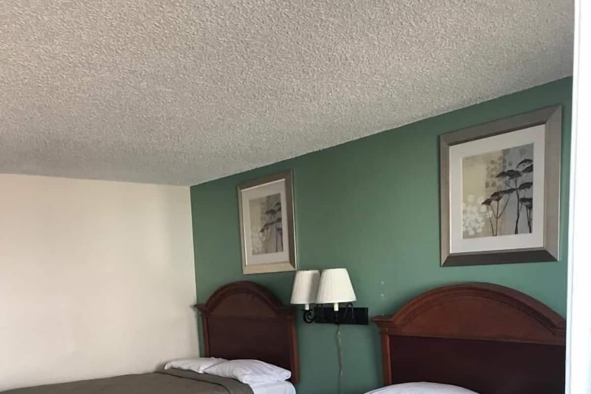 A hotel room with two beds, a nightstand, a lamp, and artwork on the walls.