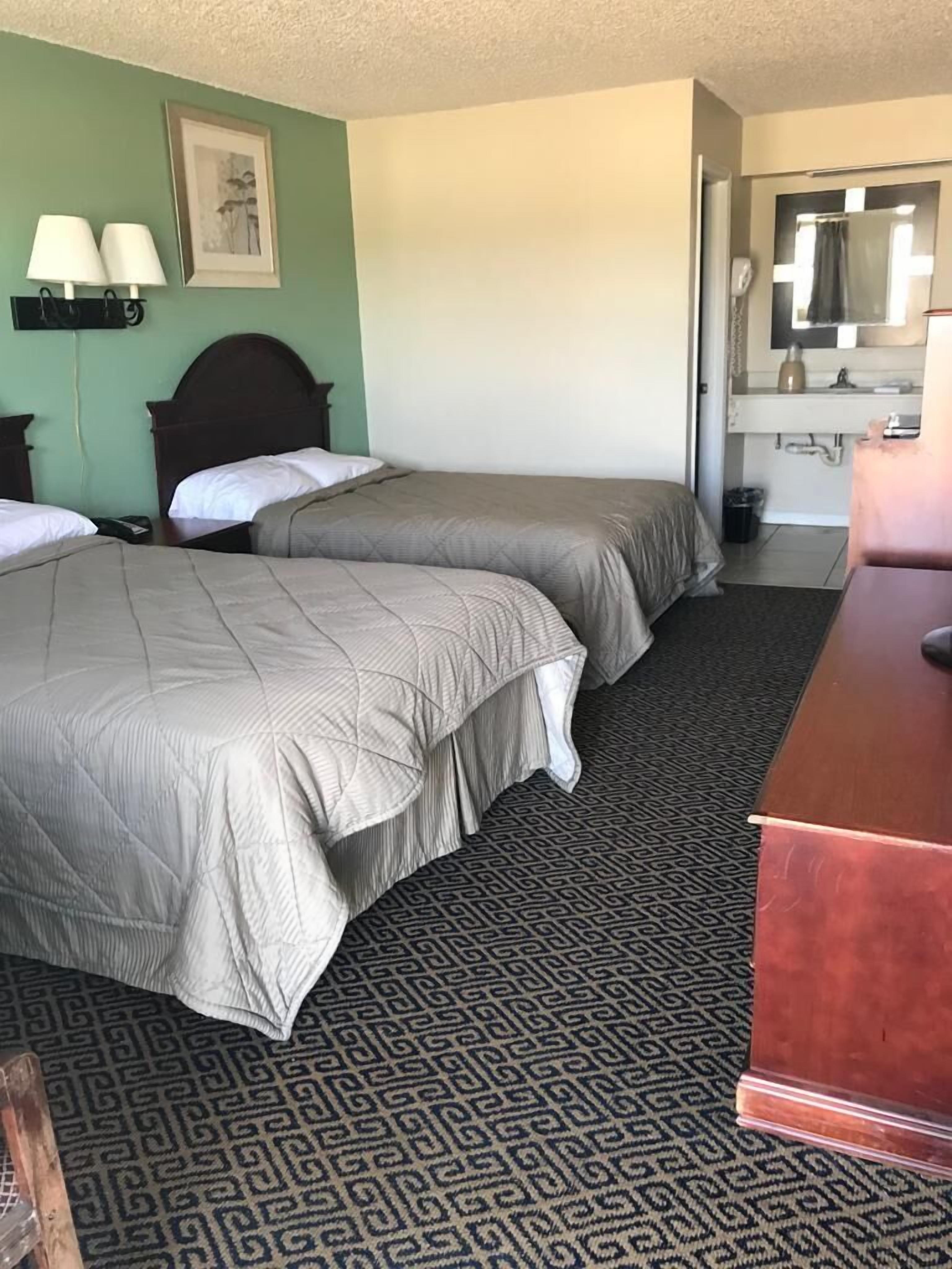 Una habitación de hotel con dos camas, un escritorio, un espejo y una alfombra estampada.