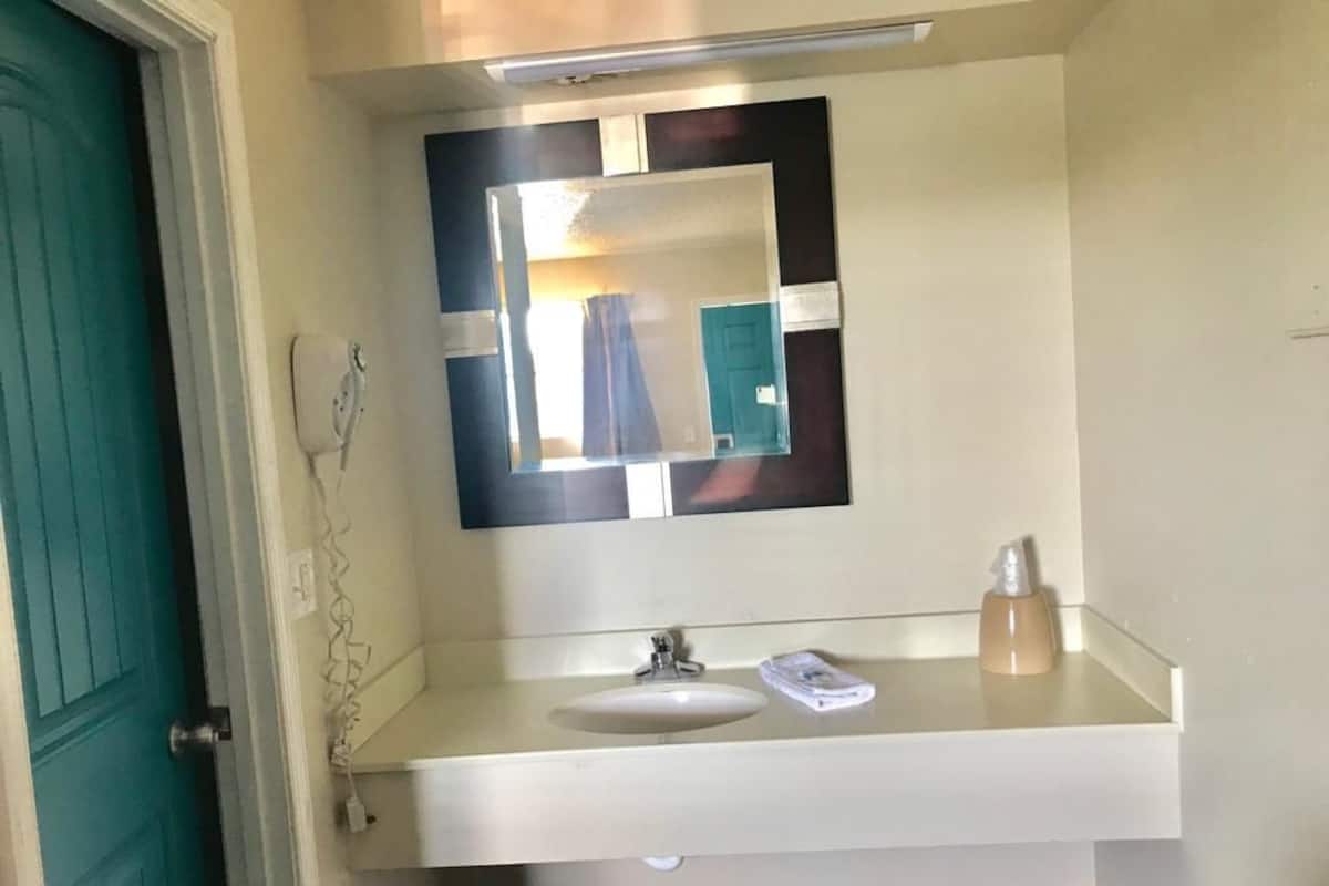 A bathroom with a white sink, a mirror, and a towel dispenser.