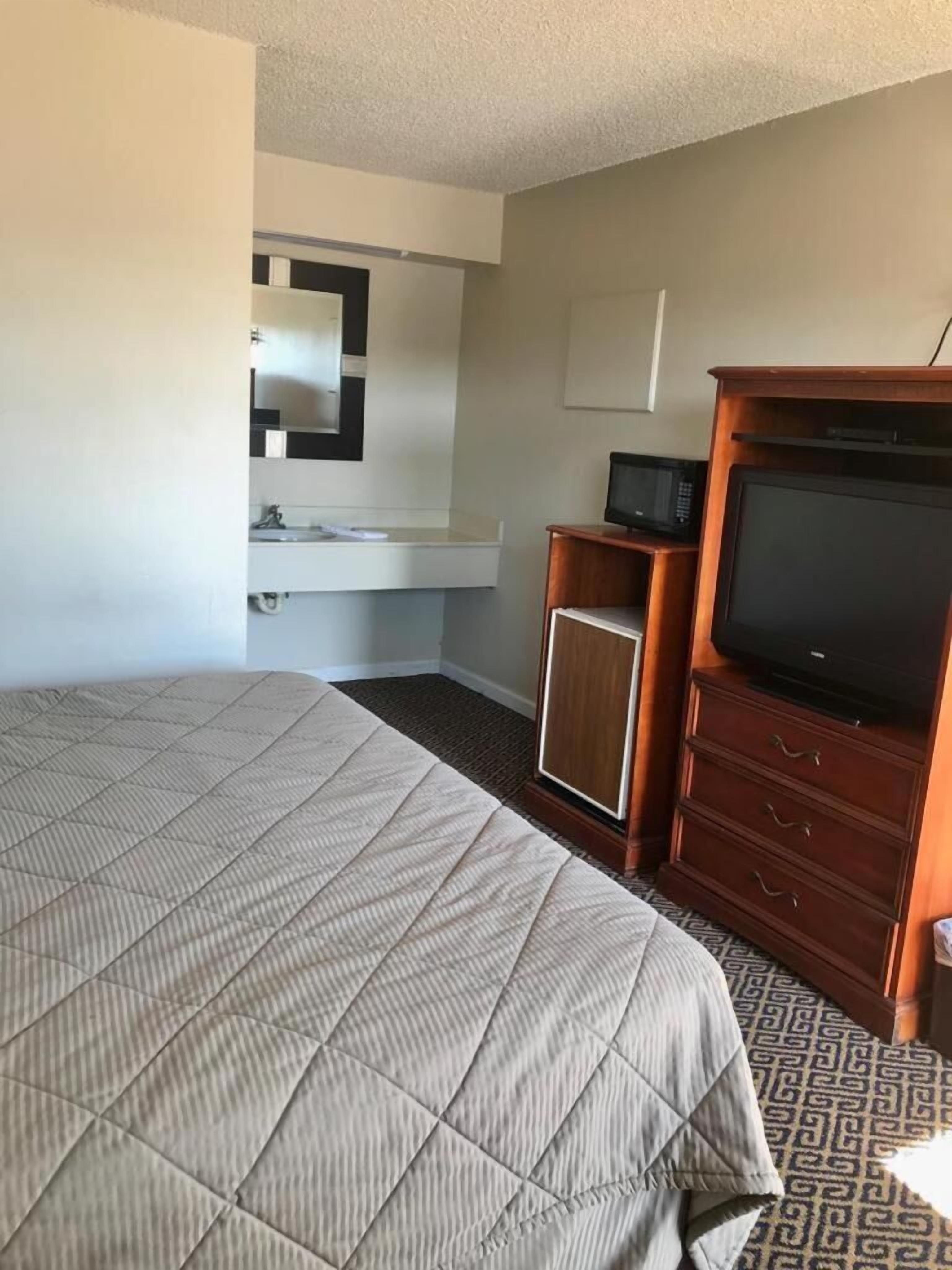 Habitación de hotel con una cama grande, un mueble de televisión de madera, un armario pequeño y un espejo en la pared.