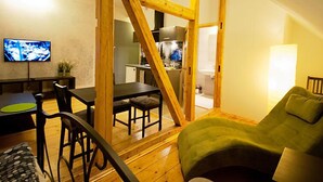Tunnelmallinen, avoimen pohjaratkaisun huone, jossa on ruokailutila, vihreä sohva ja seinälle asennettu televisio.
