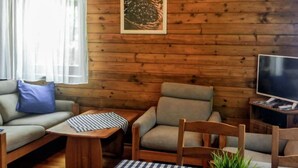 Ett mysigt rum med en väggpanel av trä, en soffa, en fåtölj, ett litet bord och en tv.