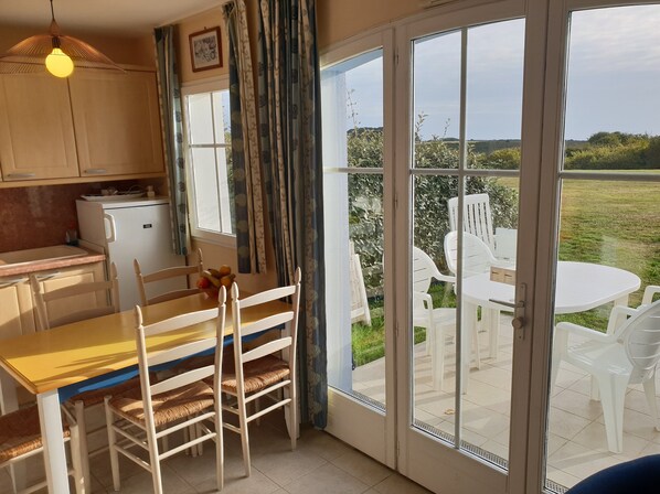 A kitchen with a refrigerator, a dining table with chairs, and a view of an outdoor patio with a table and chairs.