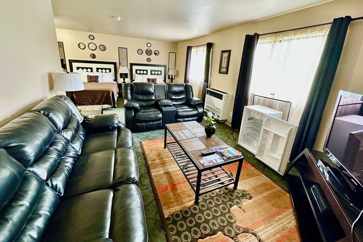 A living room with a black leather sofa, two black leather chairs, a coffee table with magazines, a small plant, and a television.