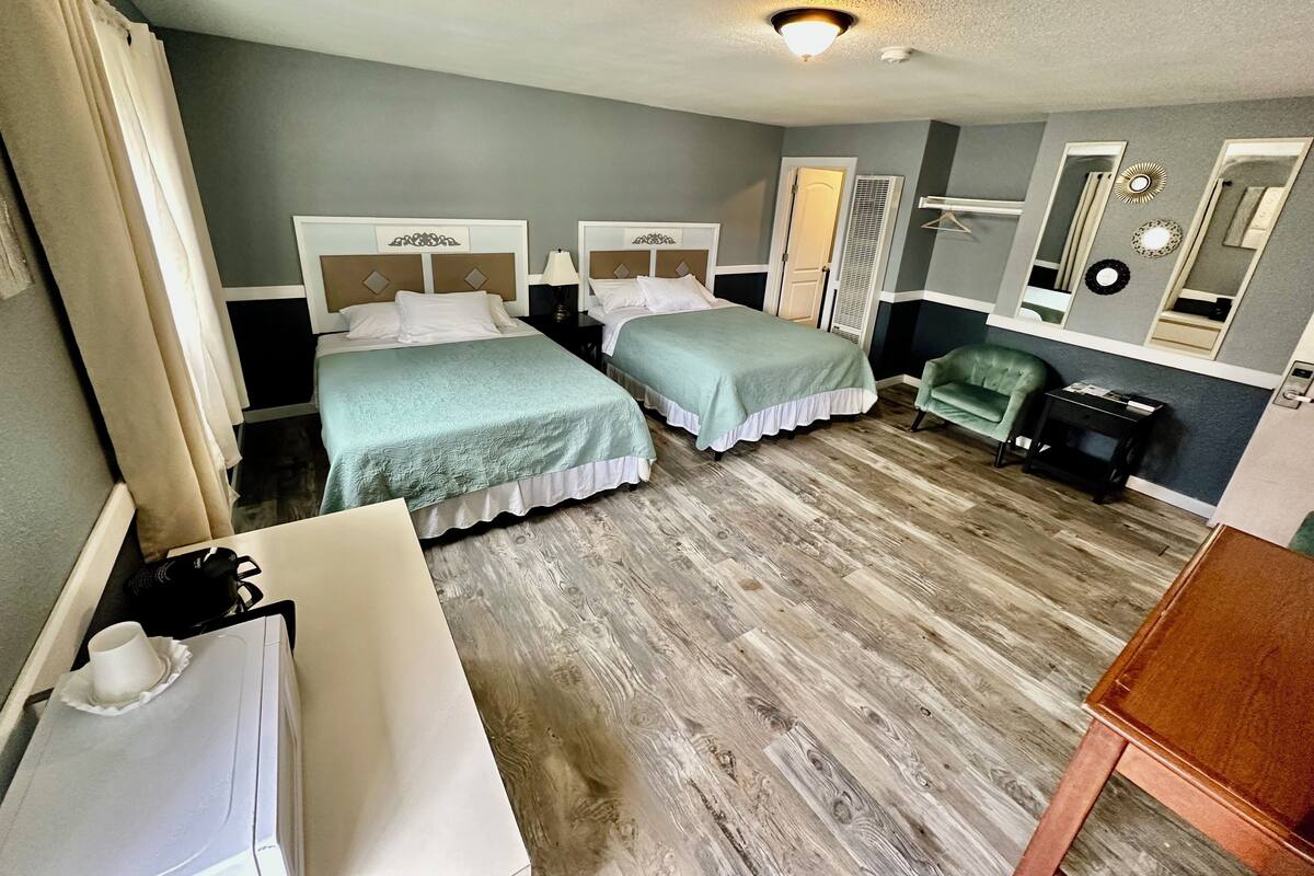 A hotel room with two beds, a desk, a chair, and a mirror.