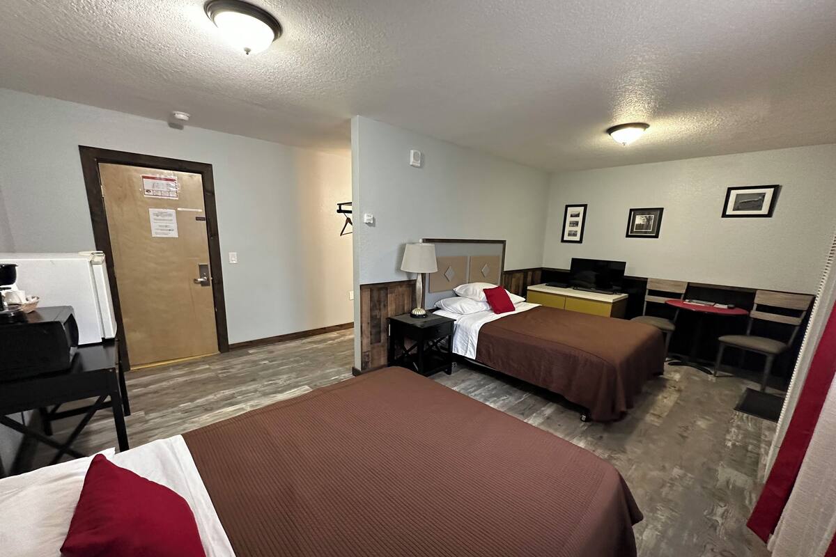 A hotel room with two beds, a desk, a TV, and a small kitchenette.