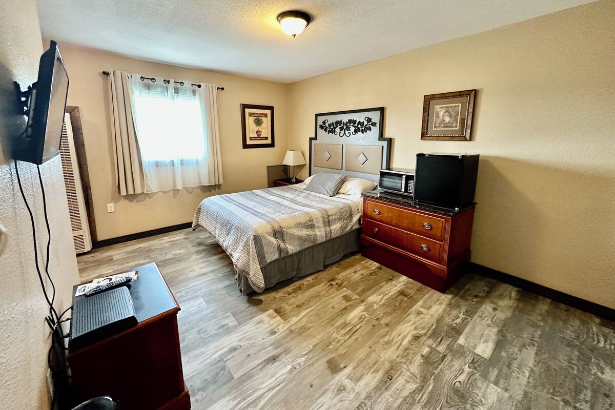 A hotel room with a bed, a TV, a dresser, and a desk with a computer.