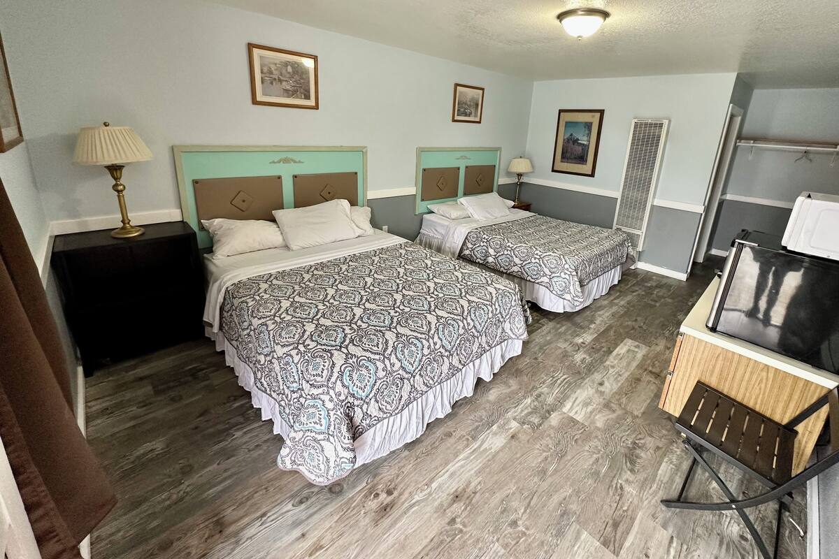 A hotel room with two beds, a desk, a chair, and a refrigerator.