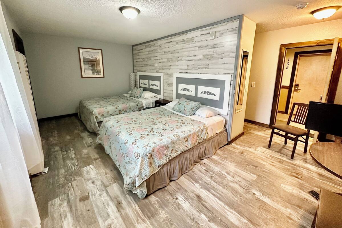 A room with two beds, a wooden floor, a desk, and a chair.