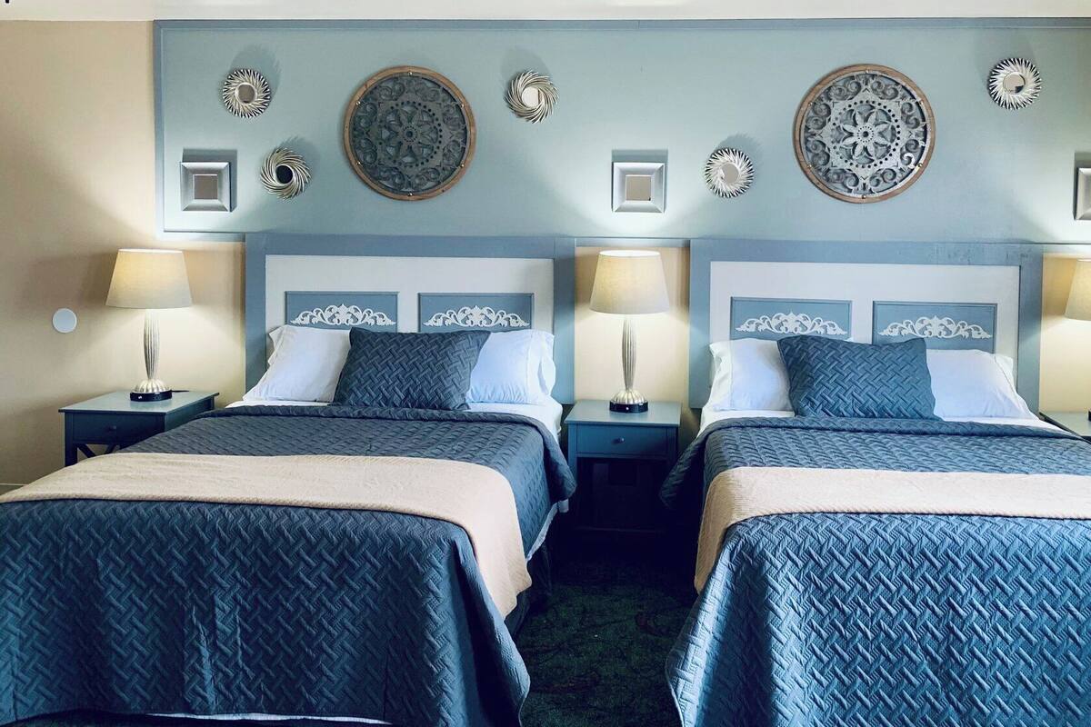 A hotel room with two beds, each with a headboard, bedside tables, lamps, and decorative wall art.