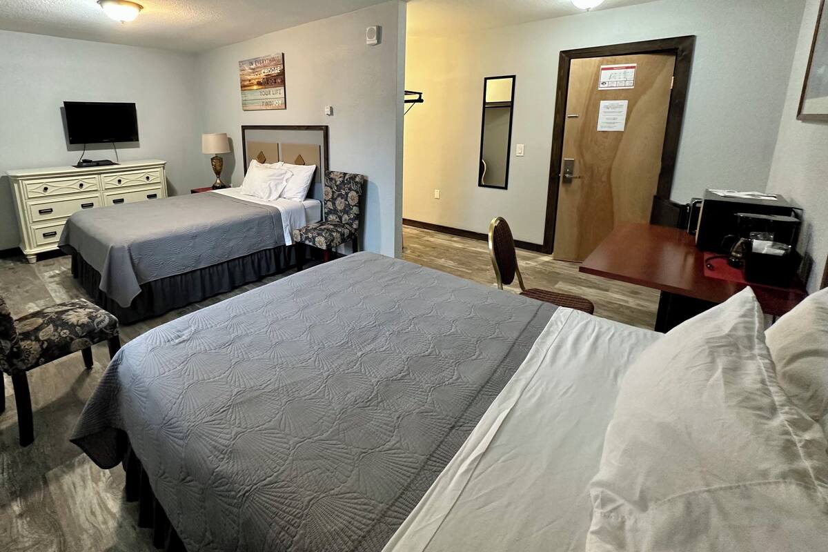 A hotel room with two beds, a dresser, a TV, a desk, and a door.