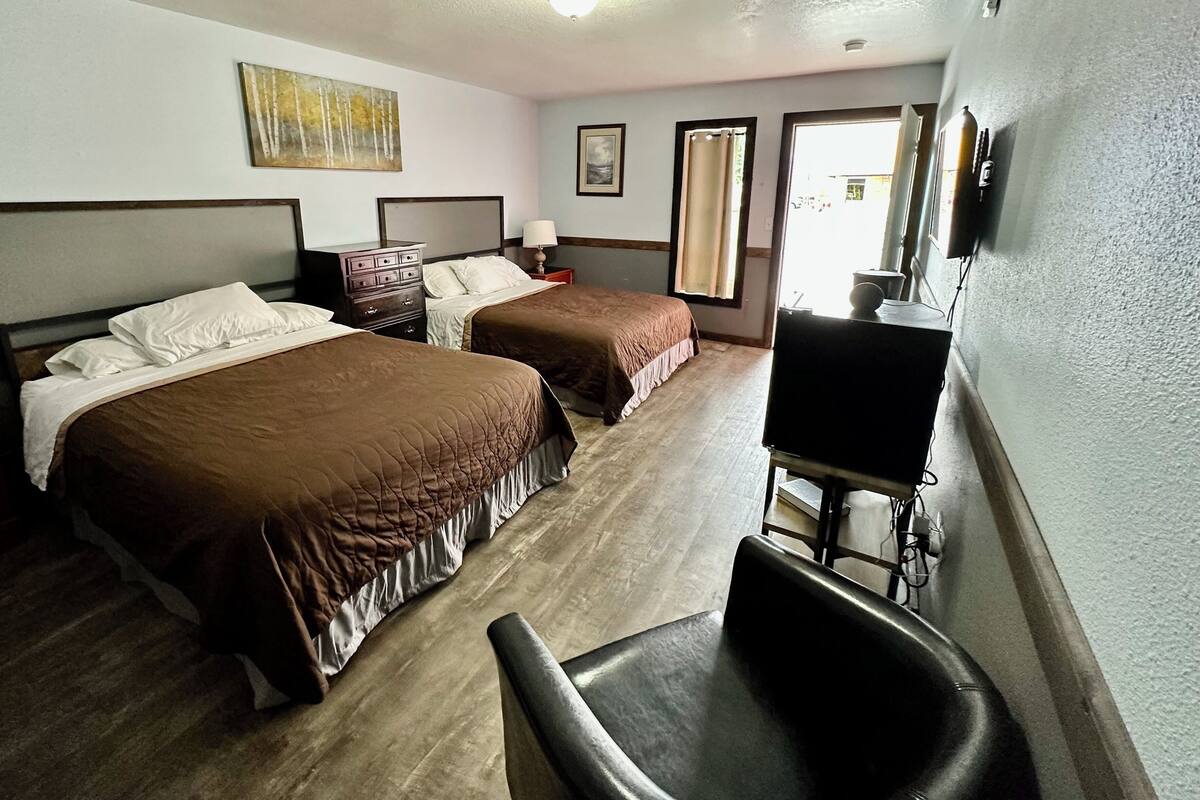 A hotel room with two beds, a desk, a chair, a TV, and a painting on the wall.