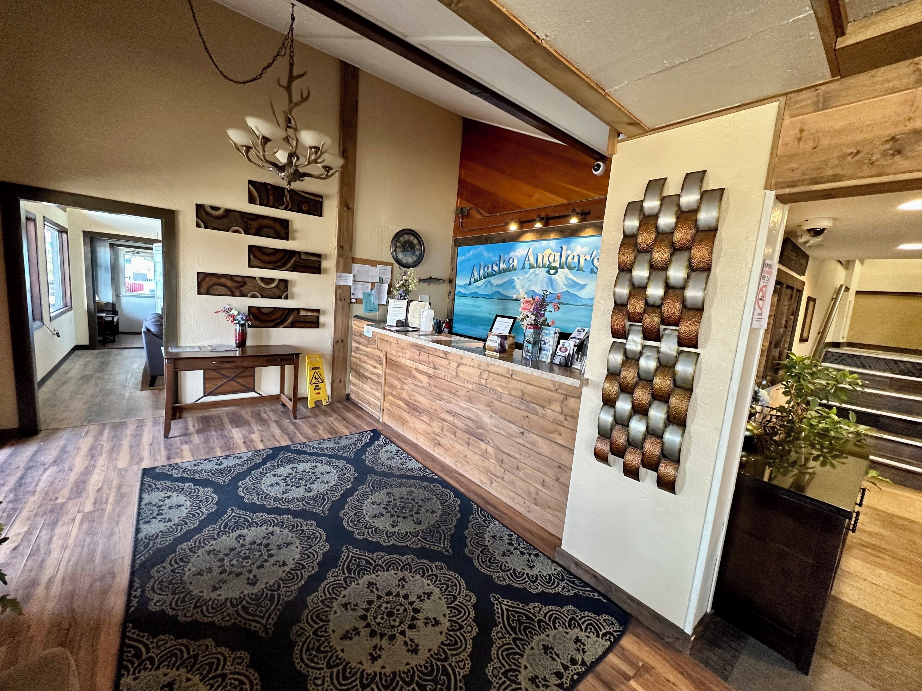 A reception area with a wooden desk, a patterned rug, a wall clock, and a large poster of Alaska.