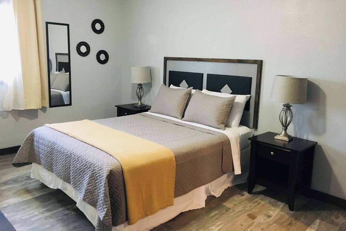 A neatly arranged bedroom with a bed, two bedside tables, a mirror, and wall decorations.