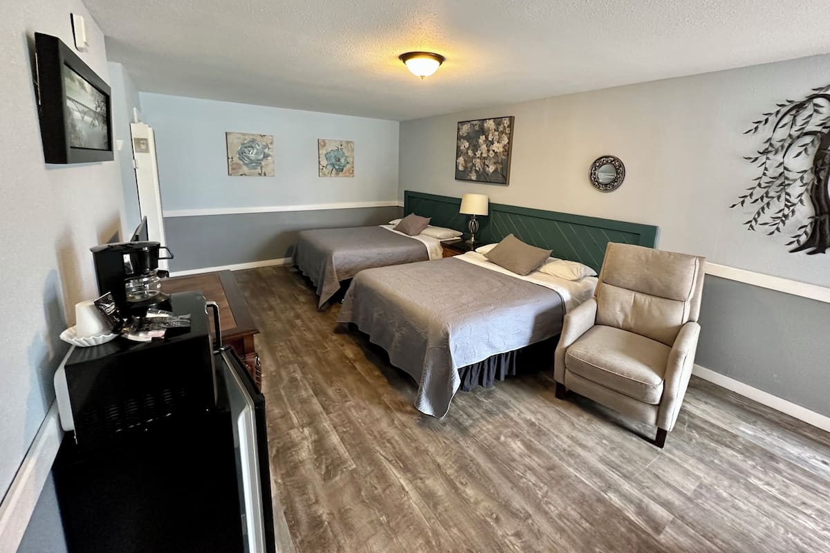 A hotel room with two beds, a chair, a coffee machine, and artwork on the walls.