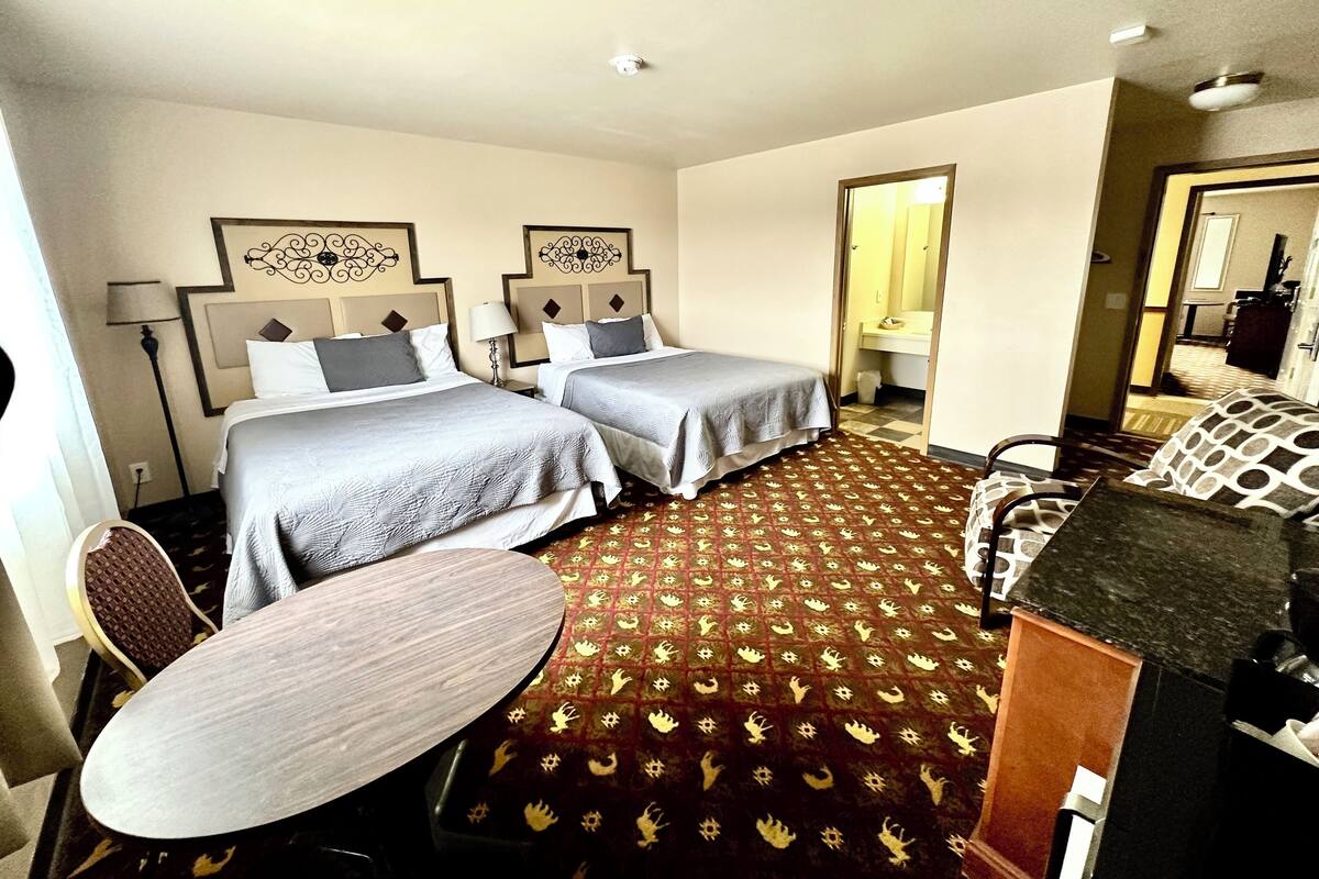 A hotel room with two beds, a desk, a chair, a patterned carpet, and a mirror.