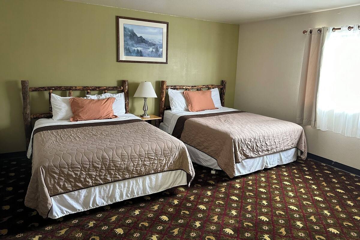 A hotel room with two beds, a framed picture on the wall, a window with curtains, and a patterned carpet.