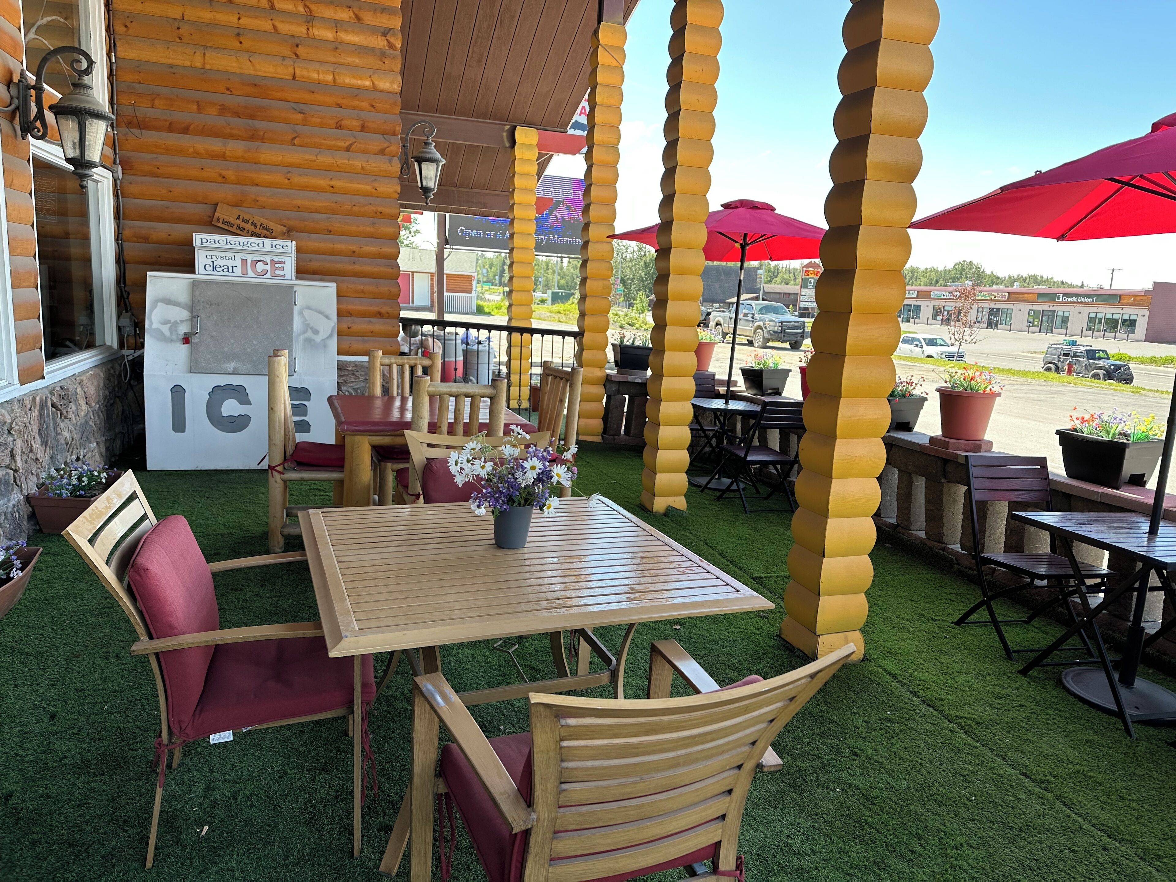 An outdoor seating area with wooden tables and chairs, surrounded by yellow pillars, and a sign advertising 'crystal clear ICE'.