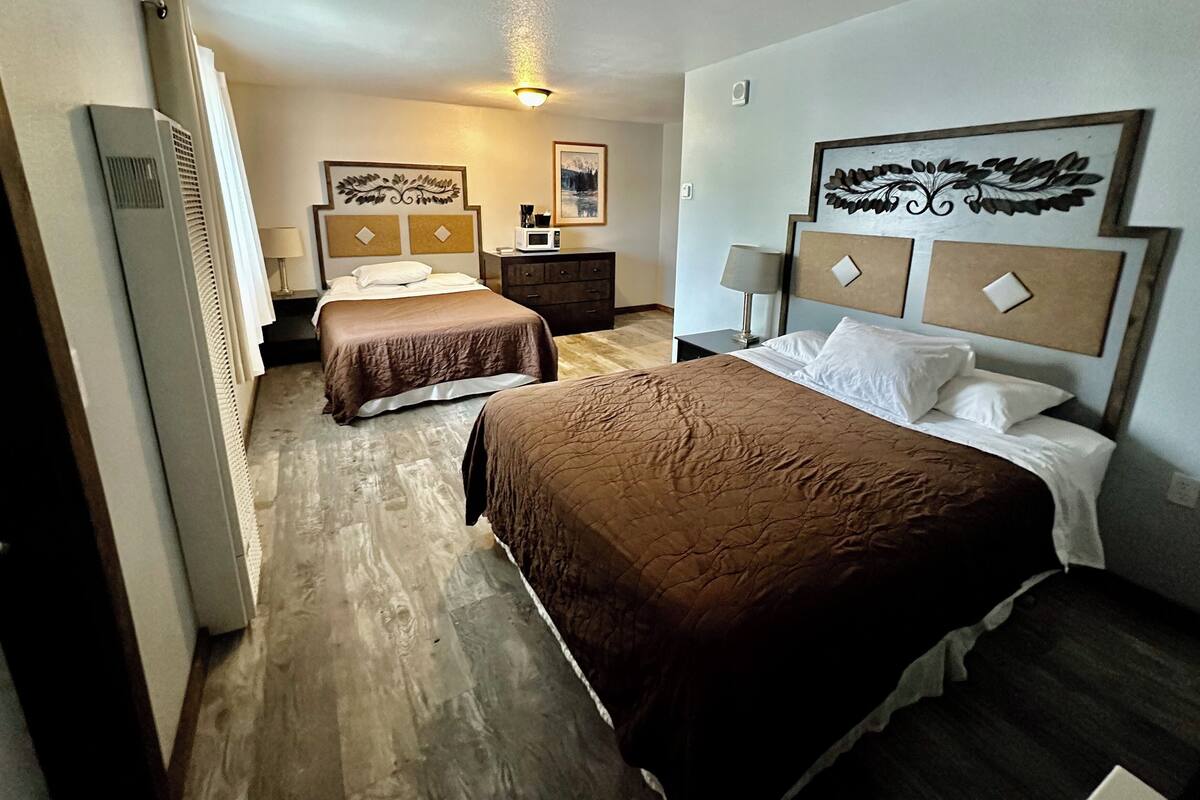 A hotel room with two beds, a dresser, a microwave, and decorative wall art.