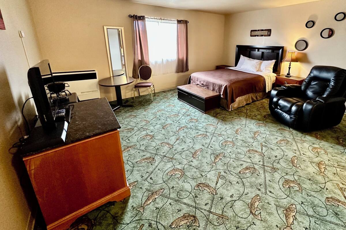 A hotel room with a bed, a desk with a coffee maker, a chair, a small table, and a mirror.