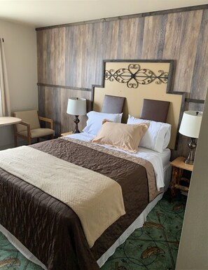 A hotel room with a large bed, two bedside tables with lamps, a chair, and a decorative wall piece. - Alaska Angler's Inn (Soldotna)