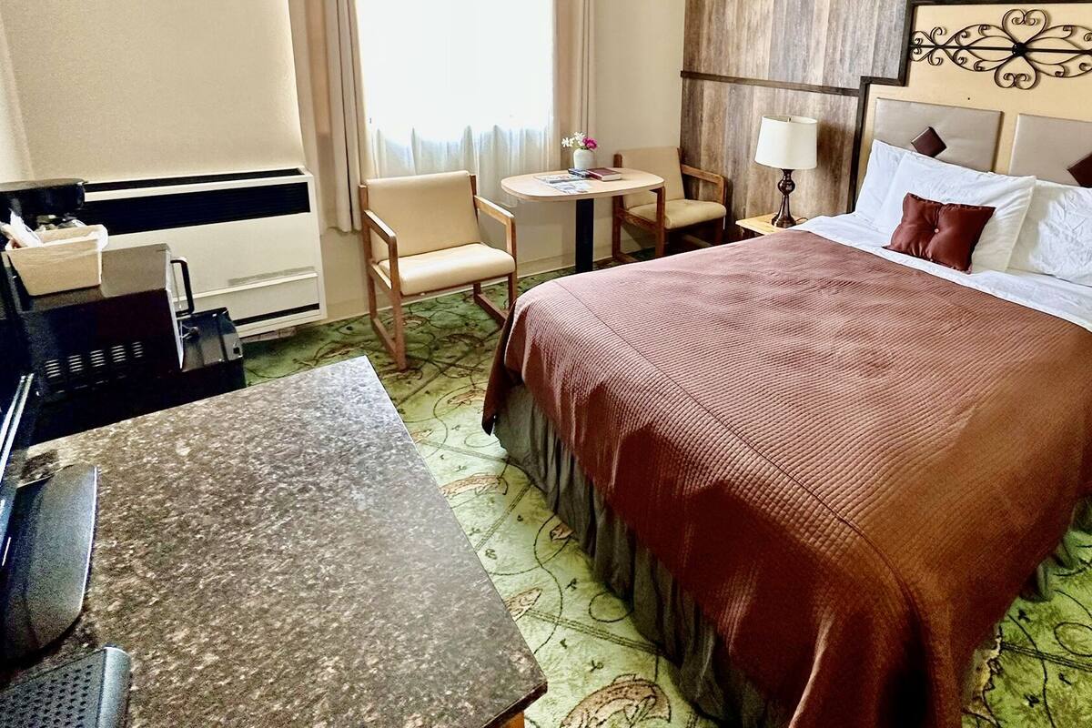 A hotel room with a bed, bedside tables, a desk, a chair, and a small table.
