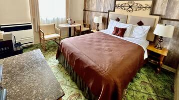 Quarto de hotel com cama, mesas de cabeceira, escrivaninha, cadeira e uma pequena mesa.