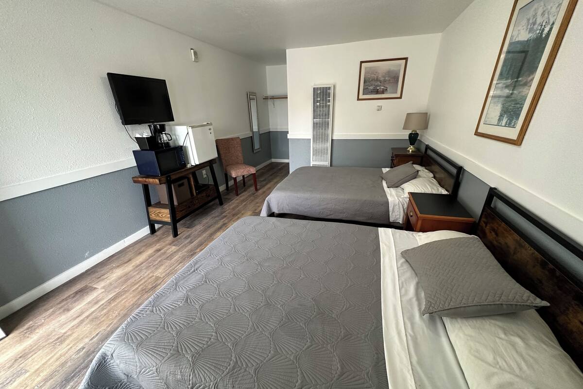 A hotel room with two beds, a TV, a desk with a coffee maker, a chair, and a picture on the wall.