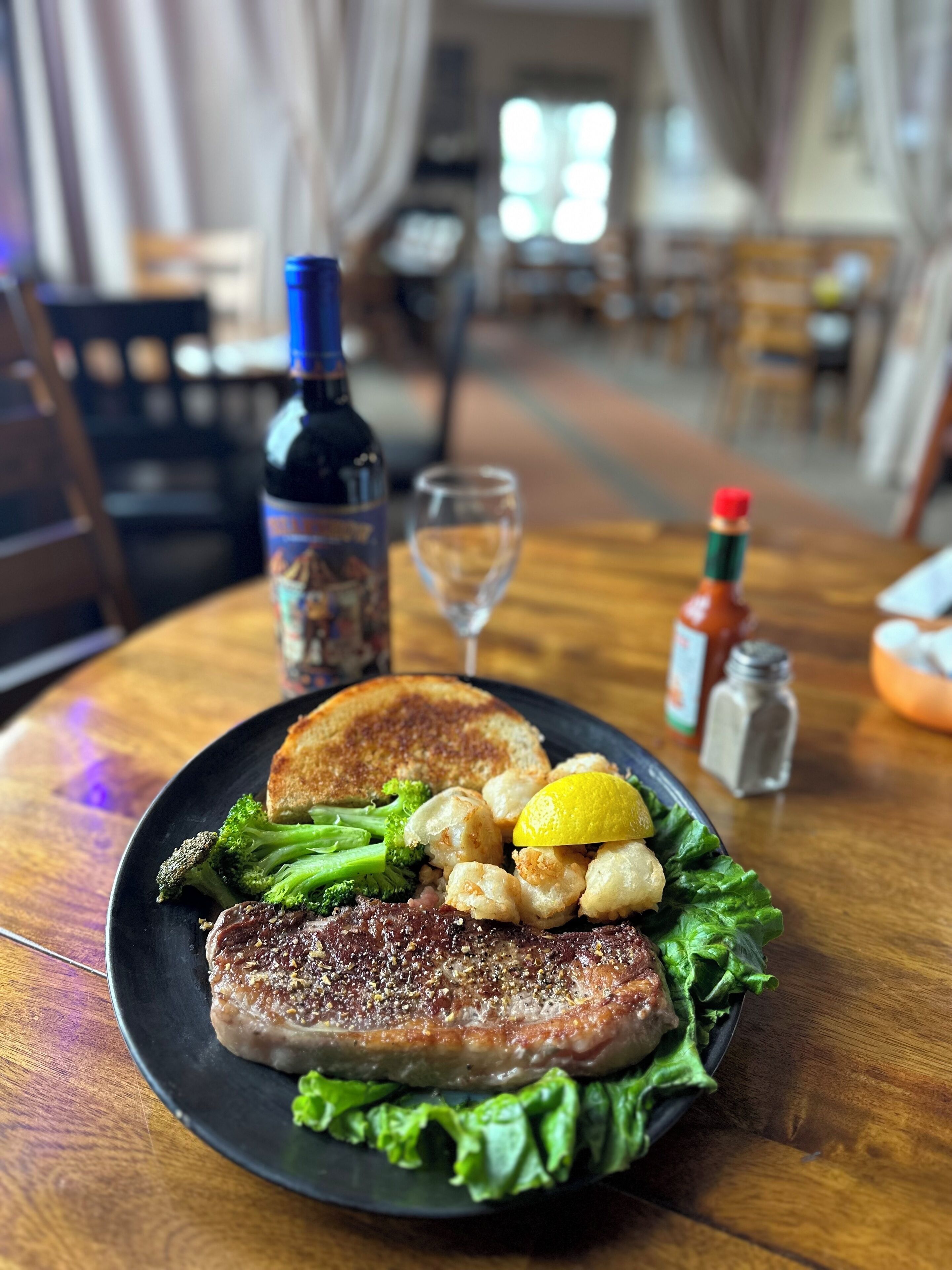 A plate of food with a steak, broccoli, and a lemon wedge on a wooden table.