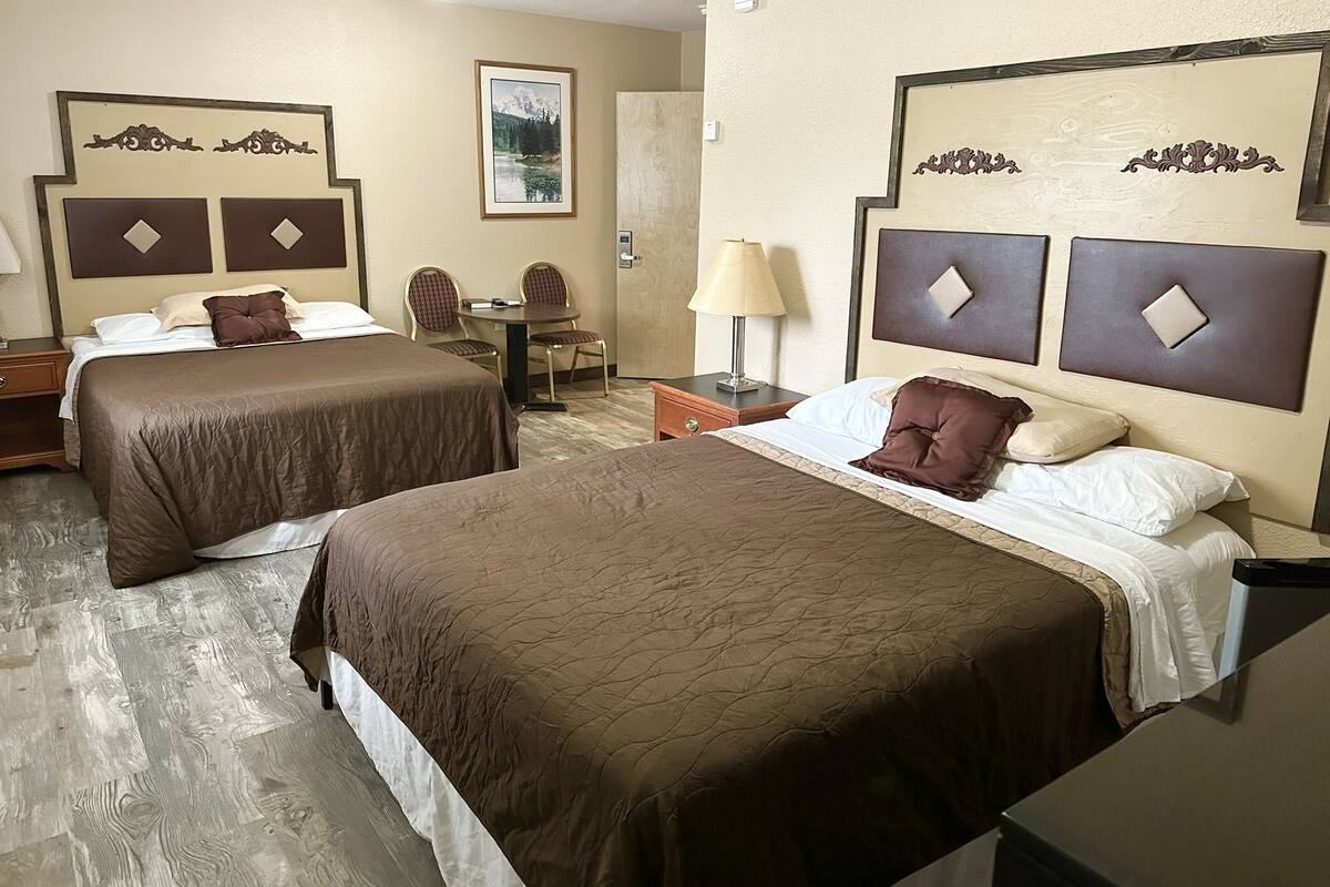 A hotel room with two beds, a desk, a chair, and a lamp.