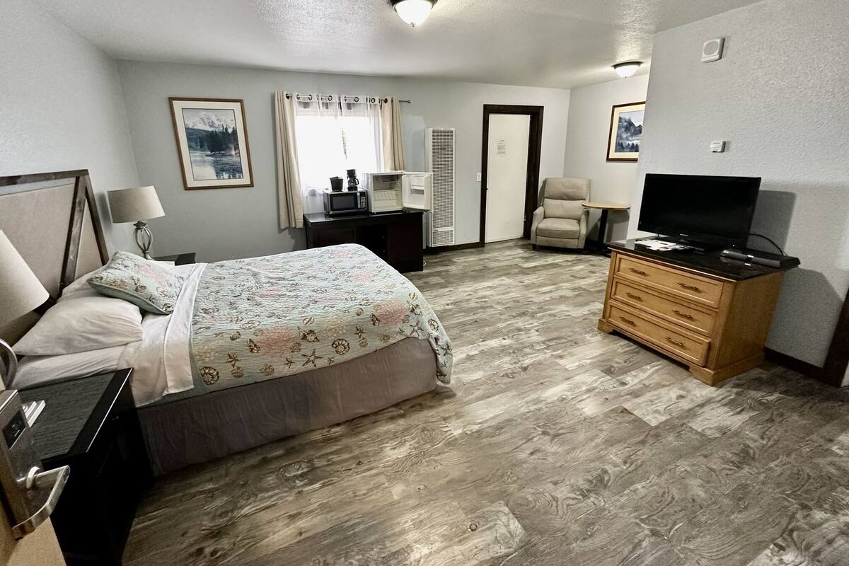 A hotel room with a bed, a desk with a lamp, a television, and a chair.