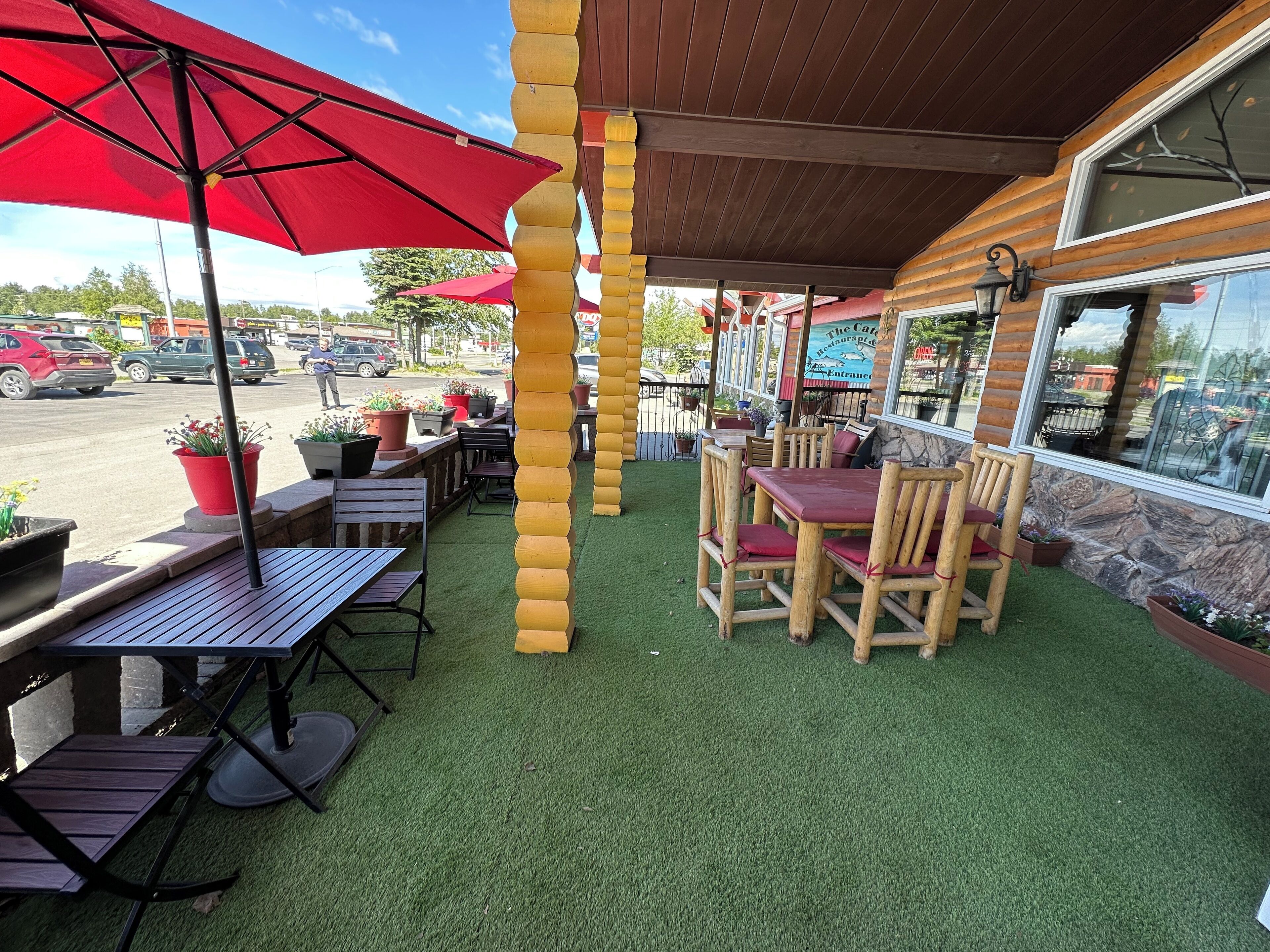 Une terrasse extérieure avec des tables et des chaises en bois, des parasols rouges et des plantes en pot.