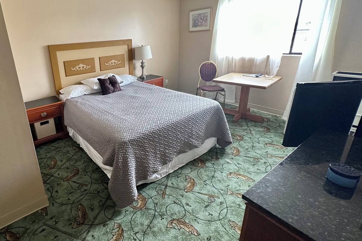 A hotel room with a bed, a desk, a chair, and a TV.