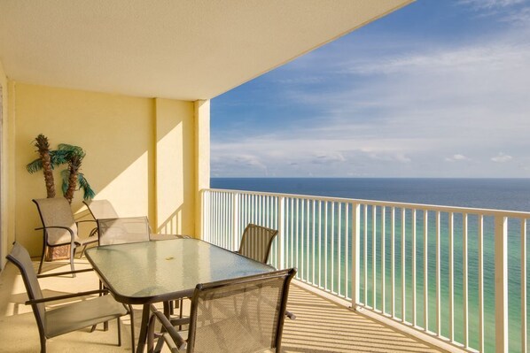 A balcony with a table and chairs, overlooking the ocean.