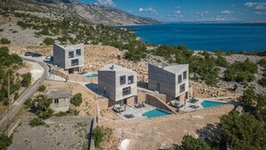 En modern villa med två stora byggnader, en swimmingpool och utsikt över havet.