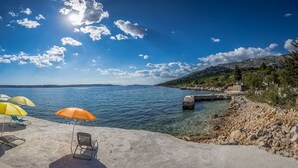 En strand med kristallklart blått vatten, en stenig kustlinje och några parasoller som ger skugga.