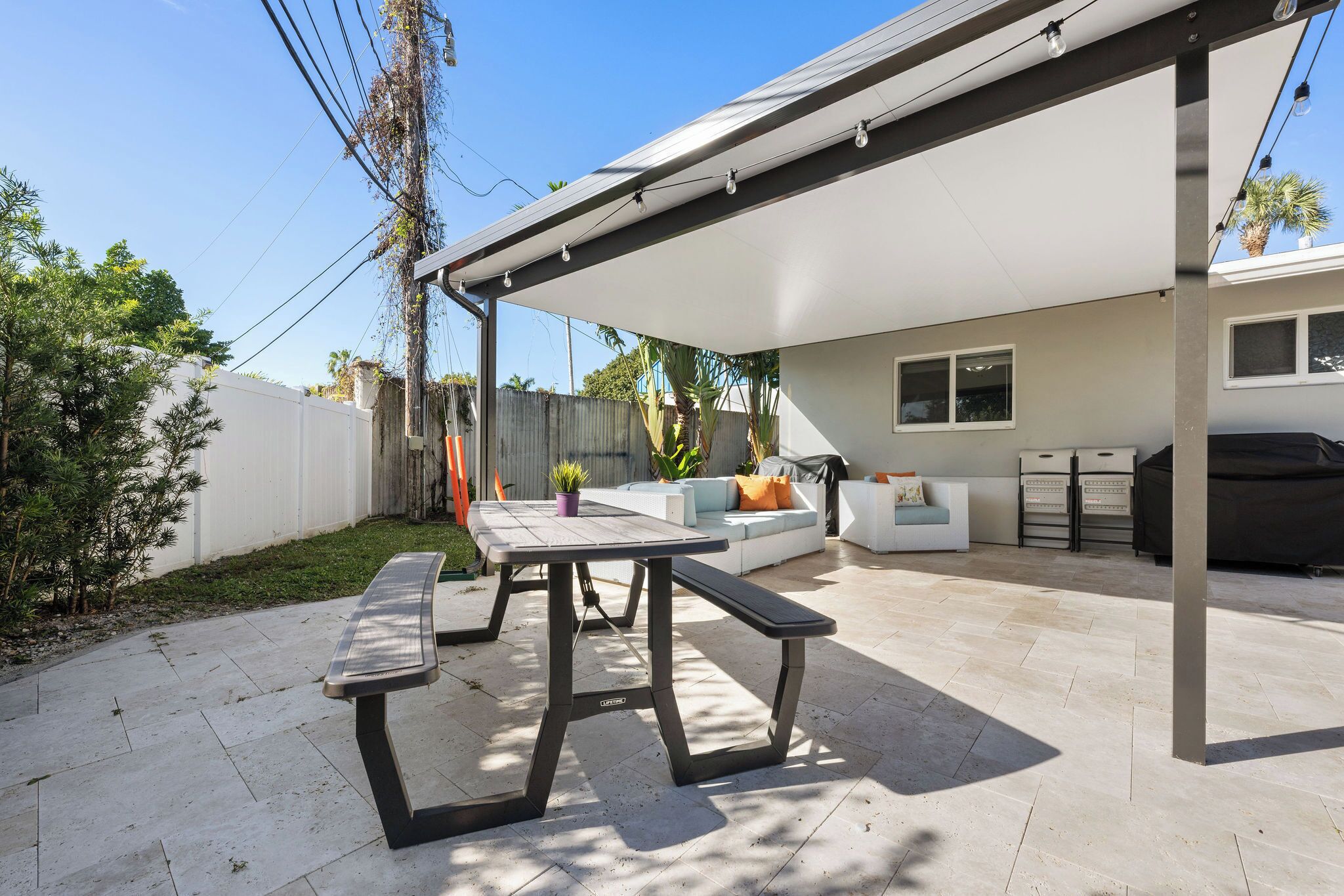 A patio area with a table and bench, a covered seating area, and a barbecue grill.