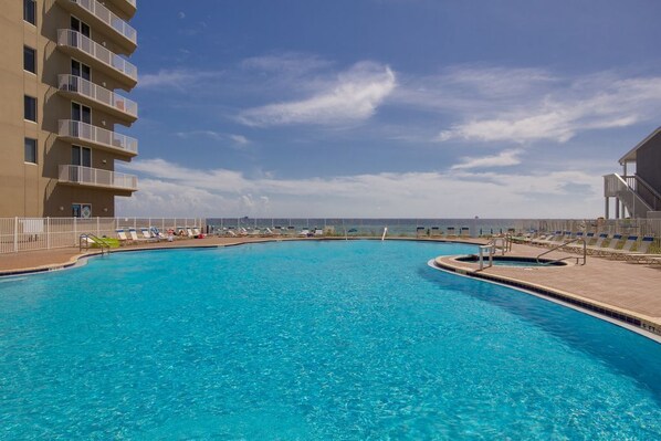 A swimming pool with lounge chairs and a building with balconies.