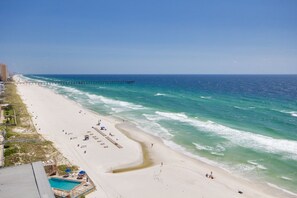 A beach with a pier extending into the ocean, a swimming pool, and beach chairs and umbrellas.