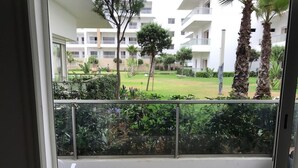 A balcony with a view of a well-maintained garden and a multi-story building in the background.