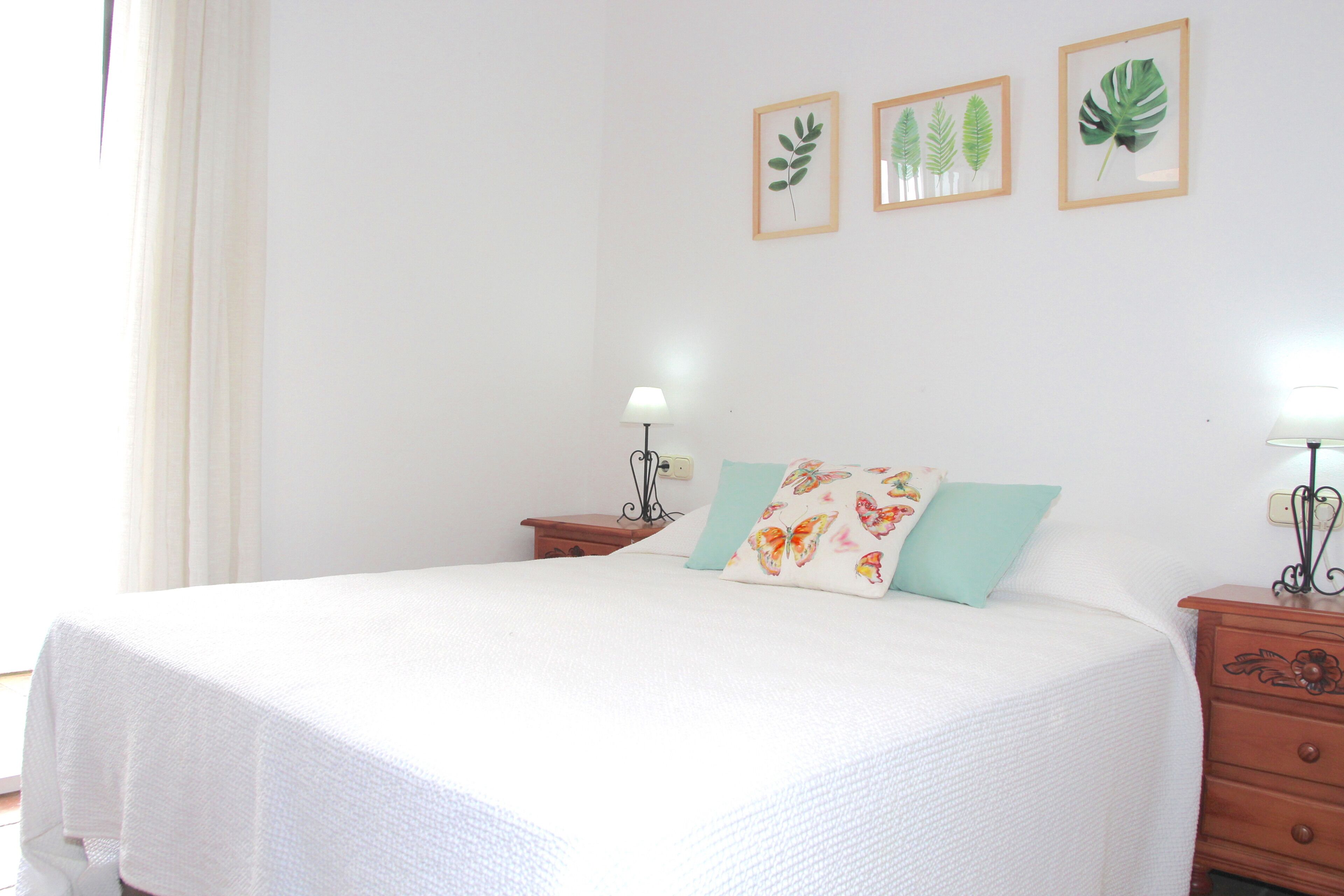 A bedroom with a bed, two bedside tables, a nightstand, and wall-mounted lamps.