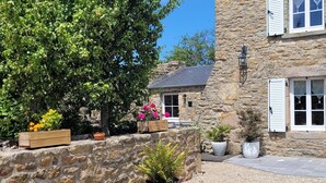 A stone building with a gravel courtyard, wooden planters with flowers, and a potted plant in the foreground. - Beautiful renovated house - 3 Bedrooms - Sea & Countryside (Maupertus-sur-Mer)