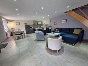Un salon moderne avec un canapé bleu, une table basse blanche et un coin repas comprenant une table et des chaises blanches.