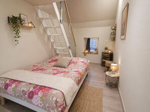 Une chambre à coucher avec un lit, une fenêtre, un bureau, une chaise, une échelle et une petite plante.