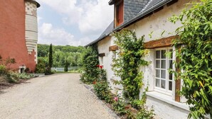 A gravel driveway leading to a white building with a red tower, surrounded by greenery and a lake view.